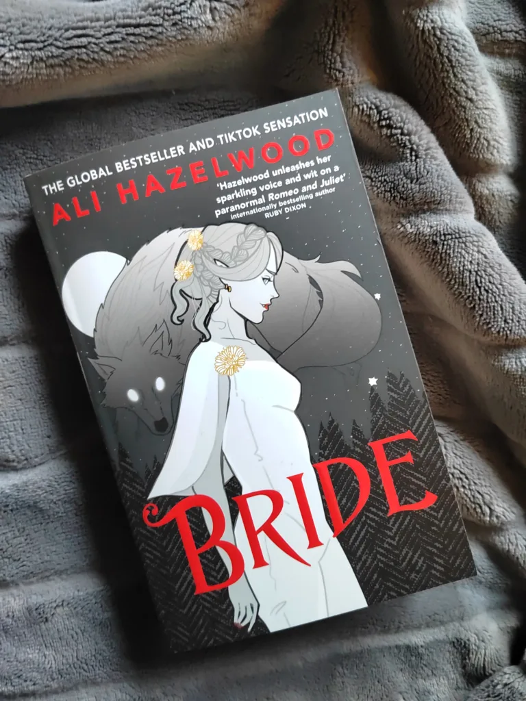A photo of Bride by Ali Hazelwood the paperback book, on a neutral gray blanket