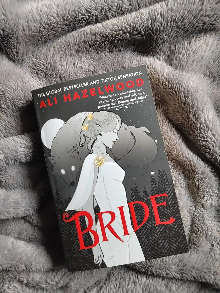 A photo of Bride by Ali Hazelwood, the paperback edition, against a gray blanket