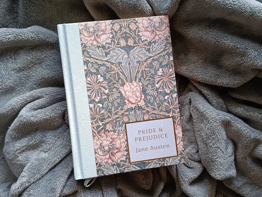 A photo of the book Pride and Prejudice by Jane Austen against a soft gray blanket. The book edition is Wordsworth Classics, the heritage collection