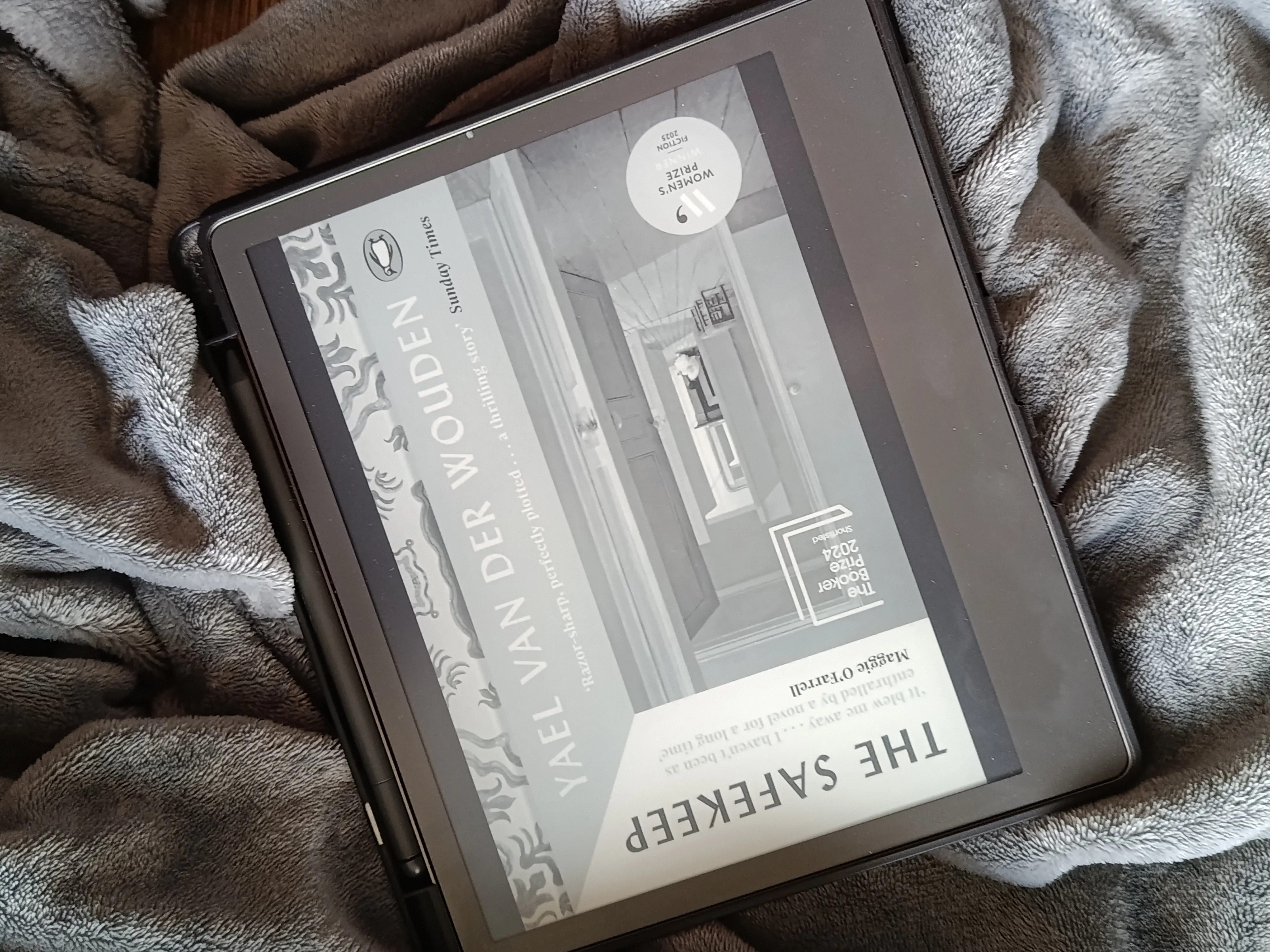 A photo of The Safekeep by Yael Van Der Wouden open on a Kindle Scribe so the cover is showing. The background is a soft gray blanket